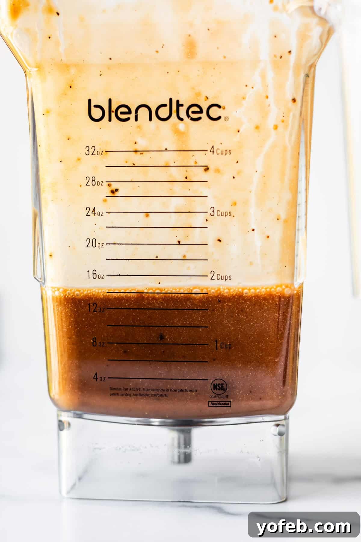 Creamy Balsamic Vinaigrette for Salads 6 A close-up of a Blendtec blender jar with a creamy light mixture on top and a brown liquid settling at the bottom, showing measurement markings up to 32 ounces and 4 cups.