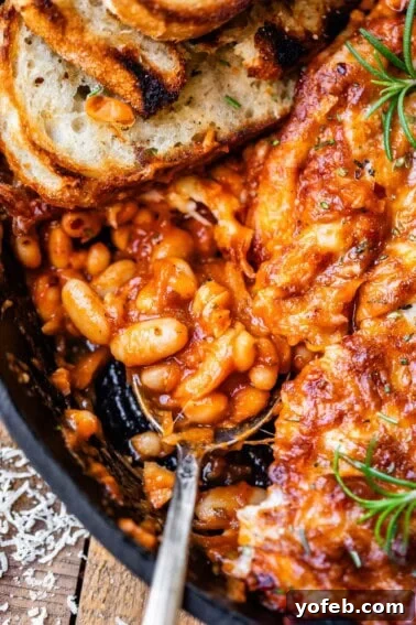 Authentic Mexican Black Beans Recipe with Garlic and Cilantro 14 metal spoon and sourdough slice stuck into a cast iron skillet of cheesy beans.