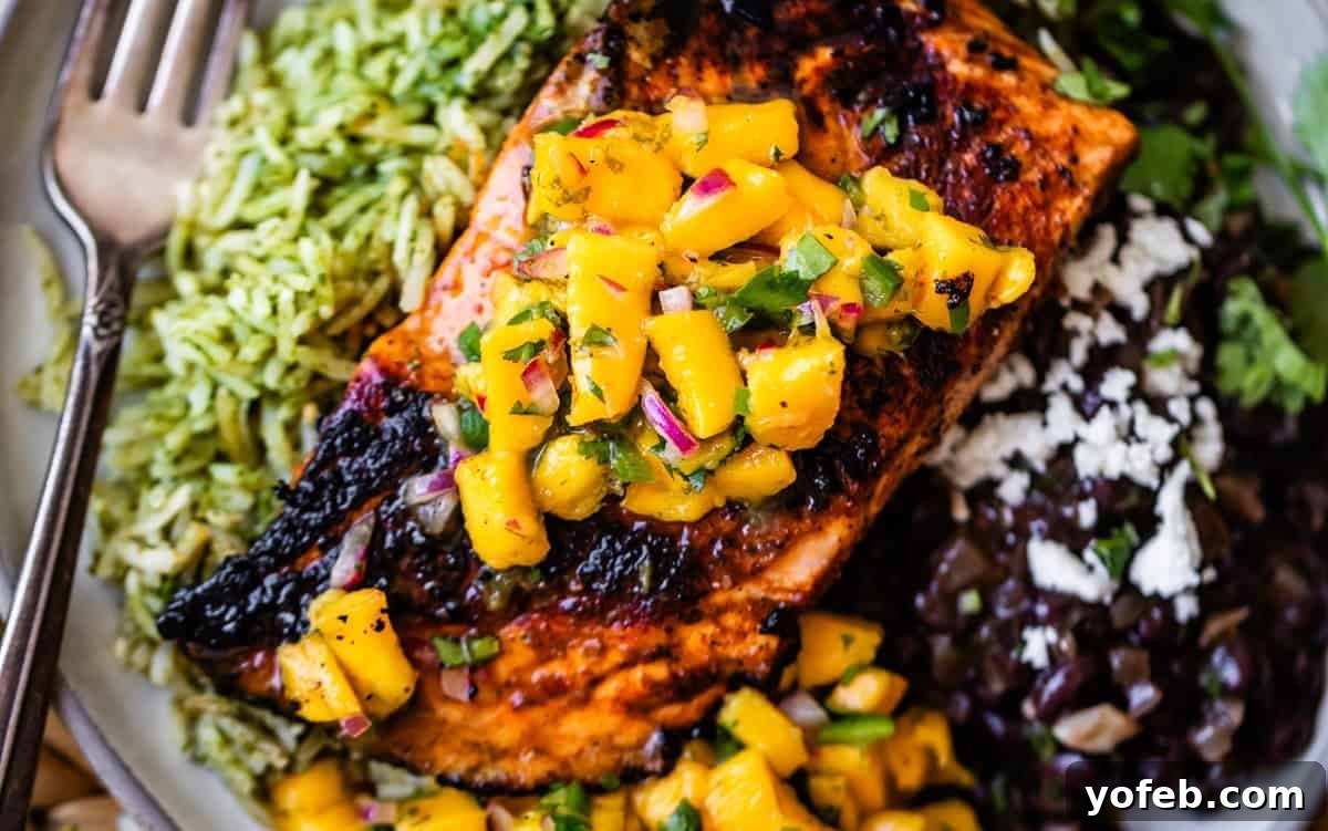 Authentic Mexican Black Beans Recipe with Garlic and Cilantro 5 Grilled salmon topped with mango salsa, served with green rice and black beans, garnished with cheese and herbs; a fork rests on the plates edge.