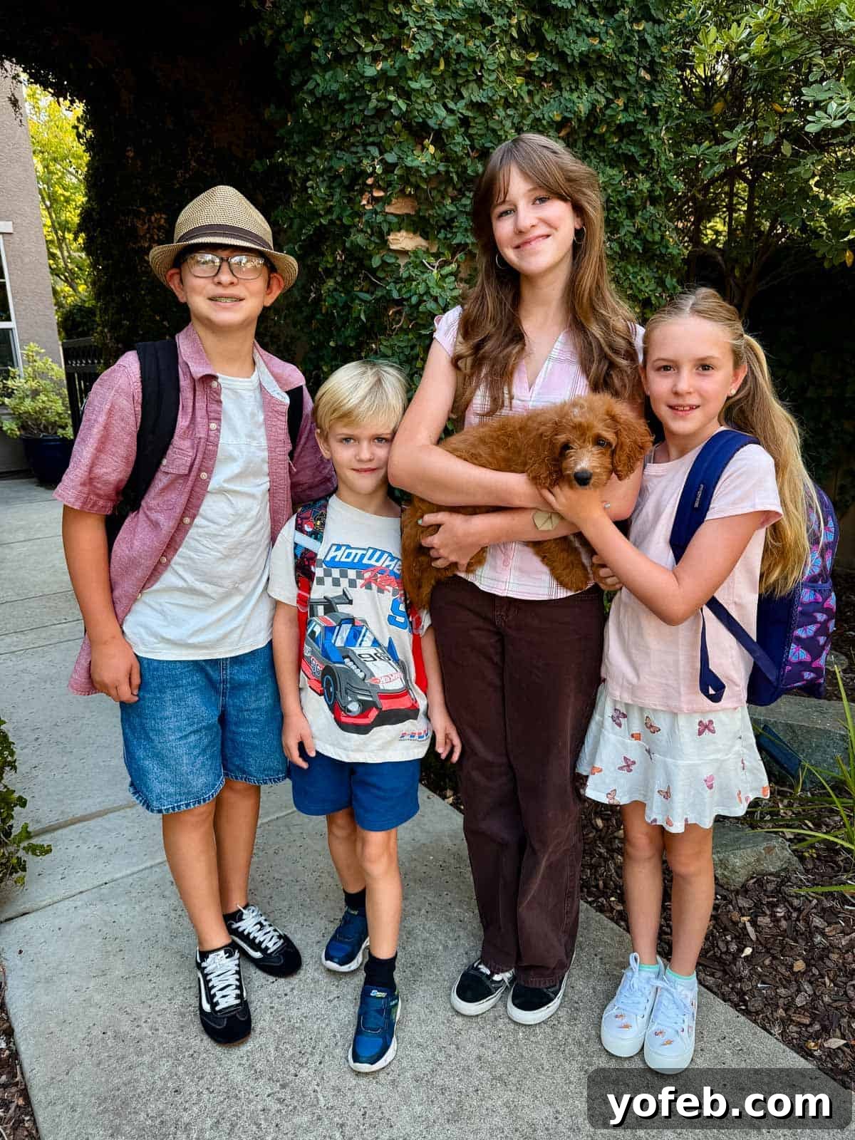 Zesty Mango Salsa Recipe with Lime and Cilantro 3 Four children stand outdoors with backpacks; one girl in the center is holding a small brown puppy. They are smiling and surrounded by greenery.