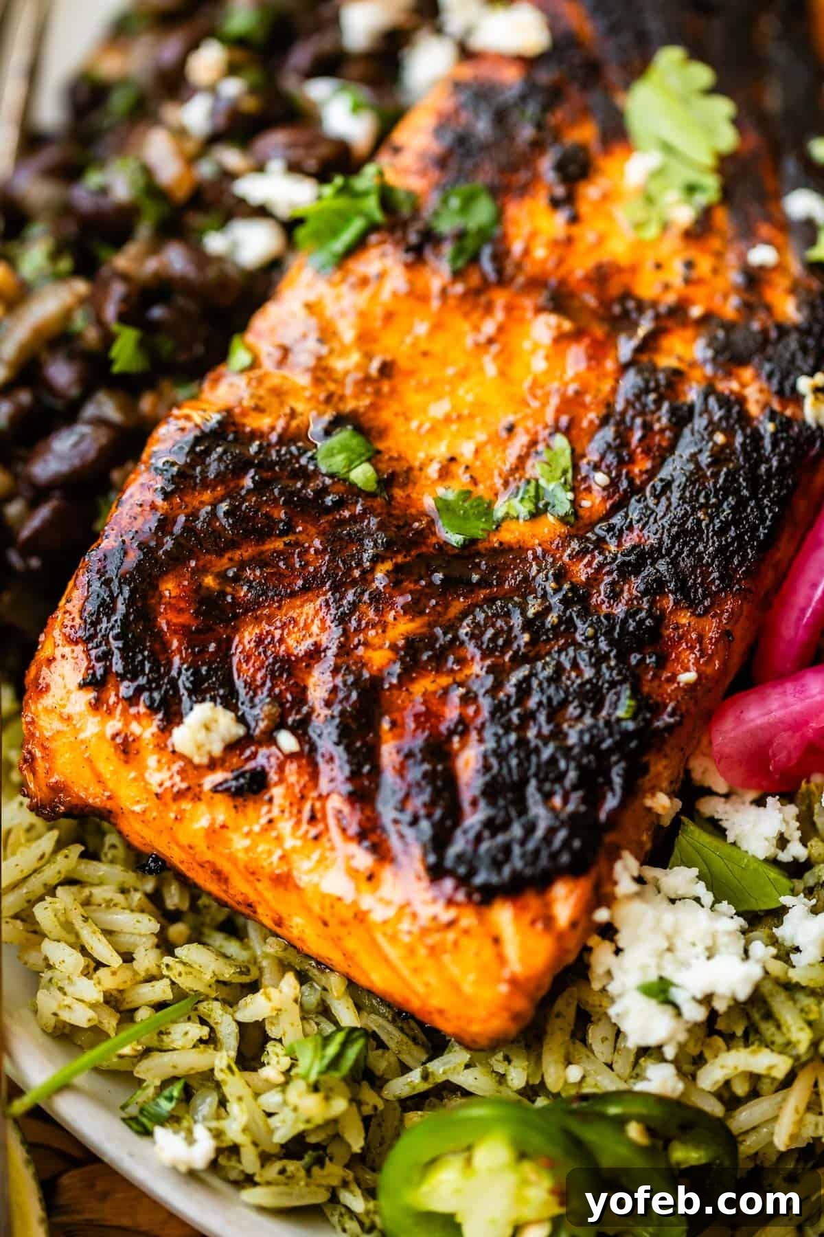 Chili-Lime Blackened Salmon 13 Grilled salmon fillet with char marks sits atop seasoned rice, garnished with cilantro, sliced jalapeños, black beans, and crumbled cheese.