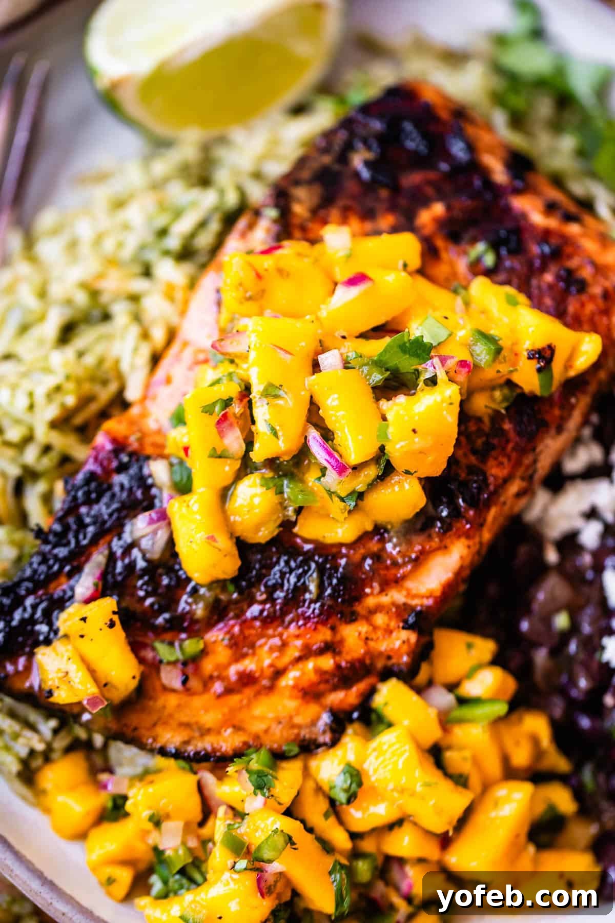 Chili-Lime Blackened Salmon 14 Grilled salmon topped with mango salsa, served with green rice and black beans. A lime wedge is in the background.