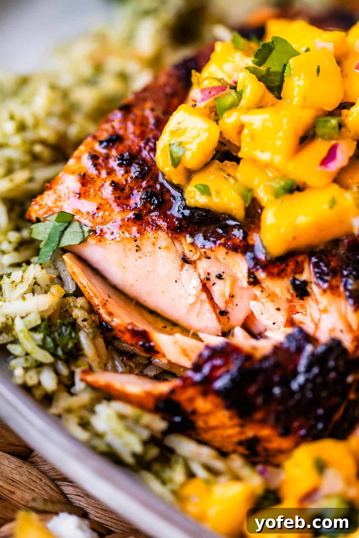 Chili-Lime Blackened Salmon 3 Grilled salmon fillet topped with mango salsa, served on a bed of herbed rice. The dish is garnished with chopped cilantro and red onion.