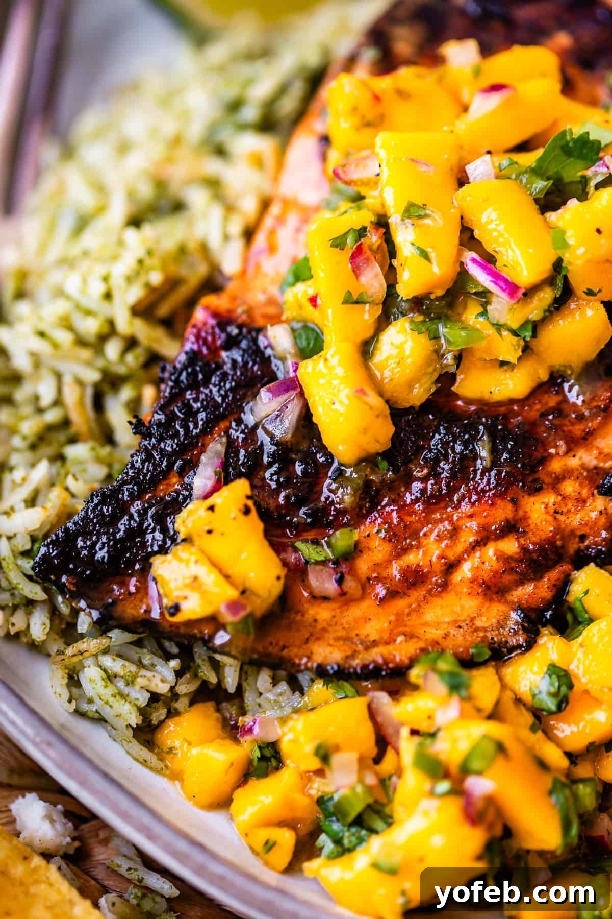 Chili-Lime Blackened Salmon 6 Grilled chicken topped with mango salsa, served with green herb rice. The salsa includes diced mango, red onion, and herbs, adding color and freshness to the dish.