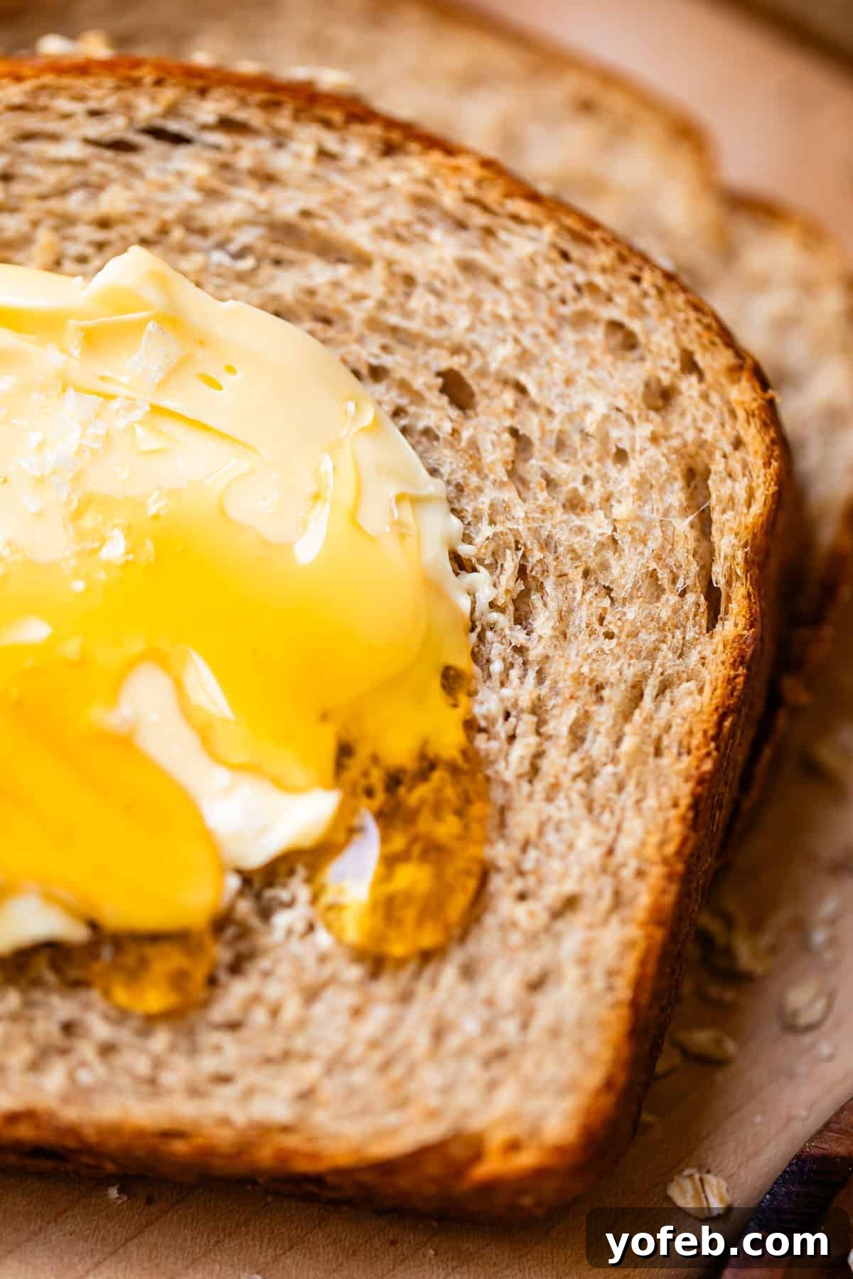 Soft Honey Whole Wheat Bread Recipe 14 A close-up of whole wheat bread topped with a dollop of butter and drizzled honey, showing the breads texture and the melting butter blending with the honey.